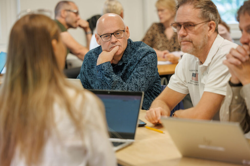 Adults in a classroom setting, focused on learning with laptops.