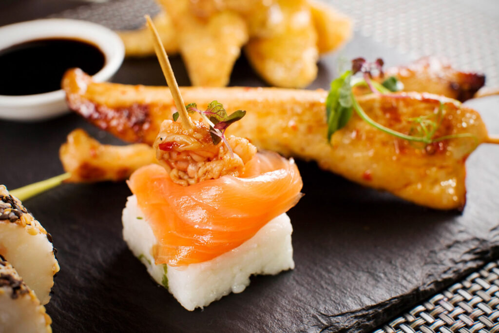 Assorted Asian appetizers: salmon sushi, shrimp, and chicken skewers.