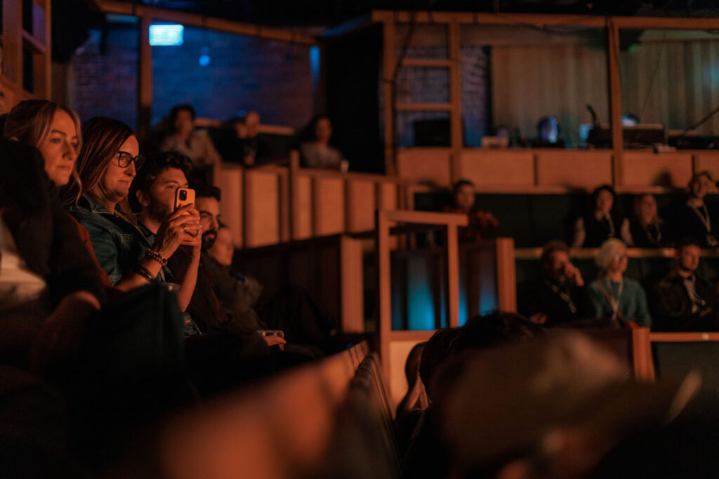Audience members watching a performance, some on phones.