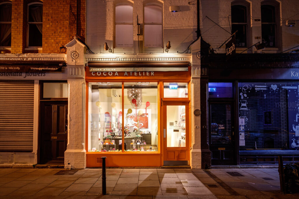 Brightly lit Cocoa Atelier chocolate shop at night.