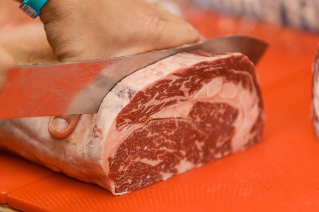 Butcher slicing marbled beef on a vibrant orange board.