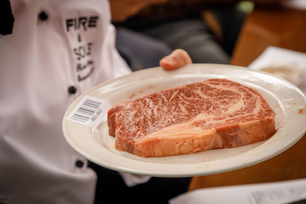 Chef holding a plate of raw, marbled steak.