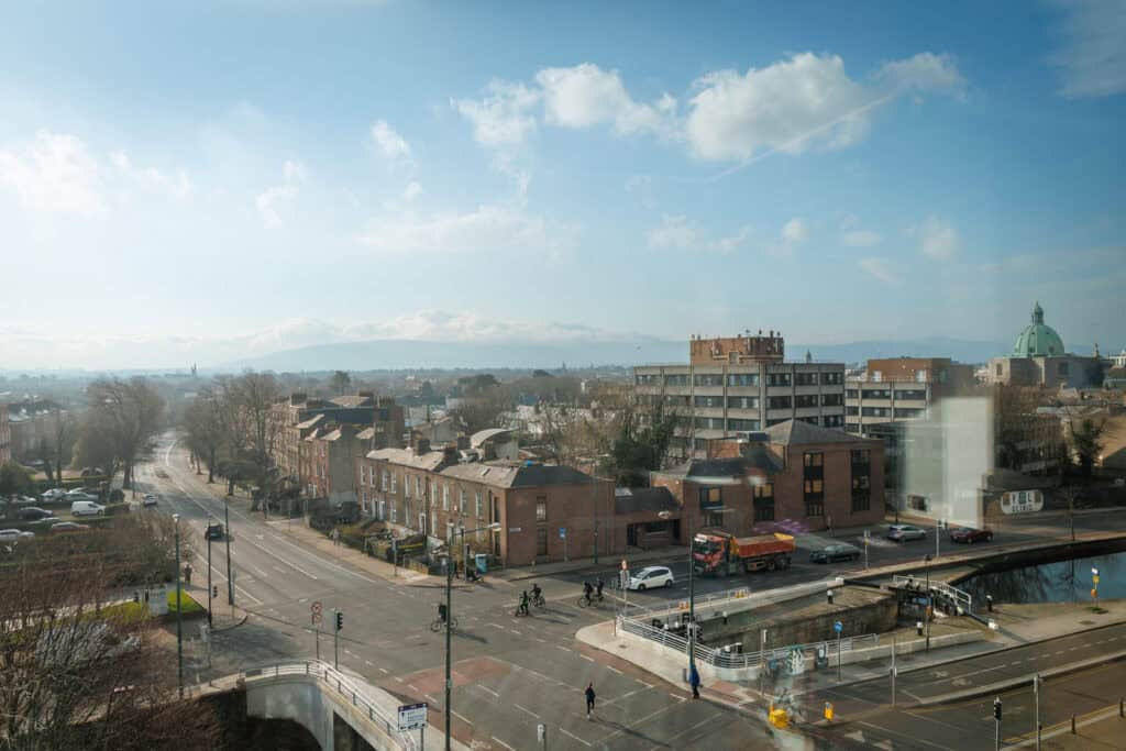 City view with canal, traffic, buildings, and distant mountains.