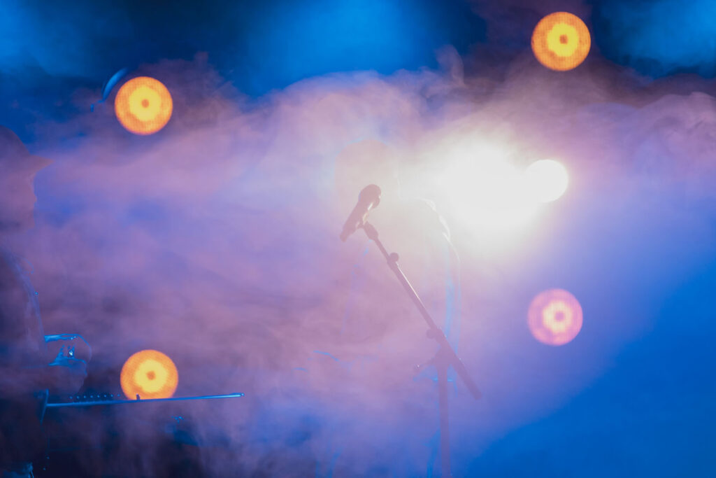 Concert stage with microphone, bright lights, and atmospheric smoke.