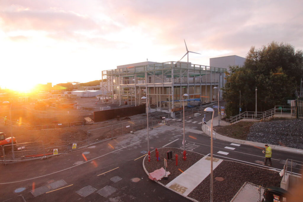 Construction site at sunset with building and wind turbine.