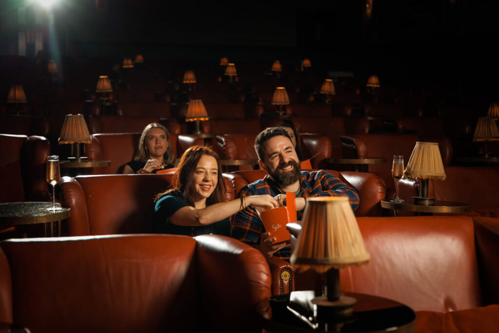 Couple happily watching a movie and sharing popcorn in a cinema.