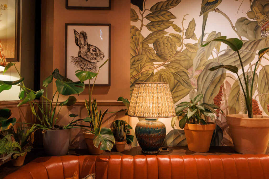 Cozy interior with plants, lamp, rabbit art, and botanical wallpaper.