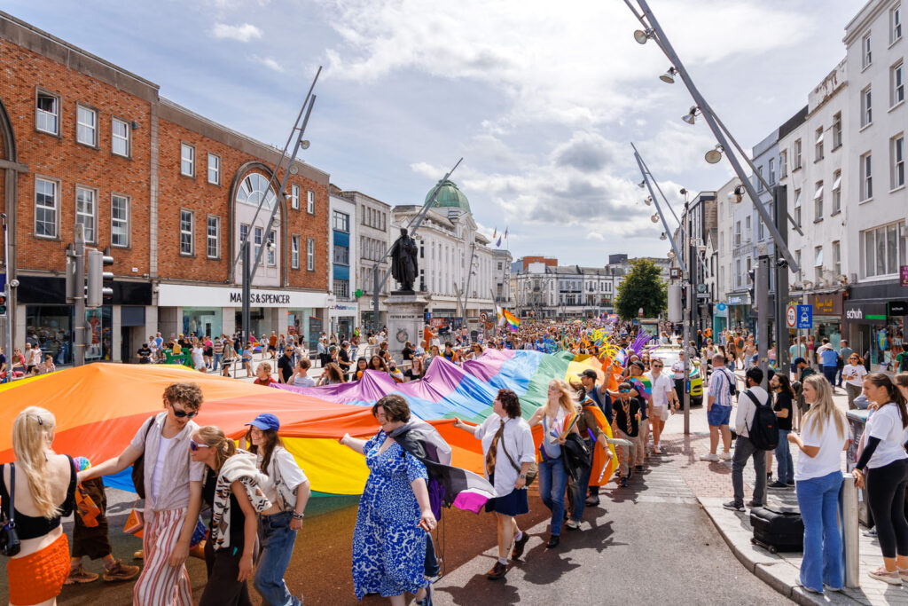 Crowd carries giant rainbow flag during Pride parade.