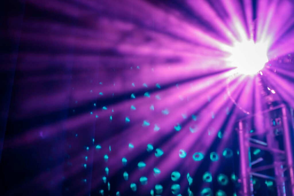 Dynamic purple light beams illuminate blue patterns.