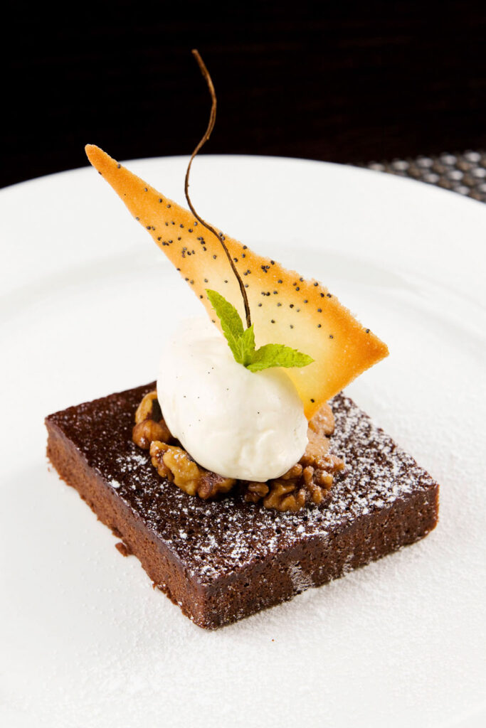 Elegant chocolate brownie with ice cream, walnuts, and poppy seed crisp.