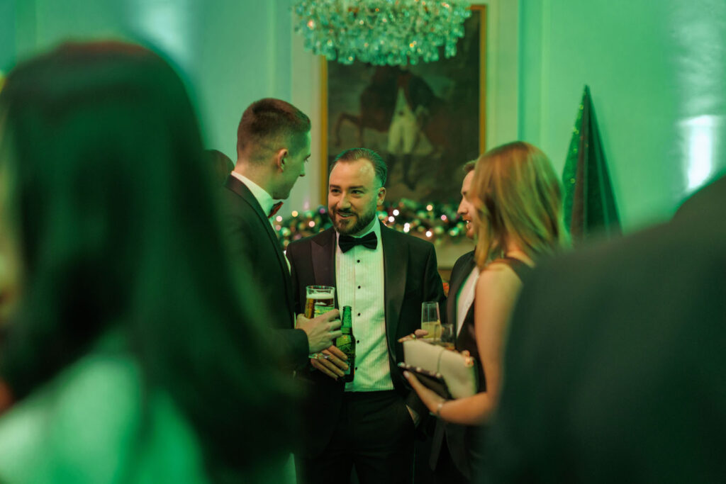 Elegant party guests enjoying drinks in a festive green setting.