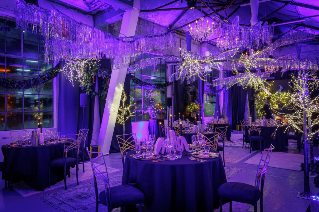 Elegant purple-lit event space with festive decorations and dinner tables.