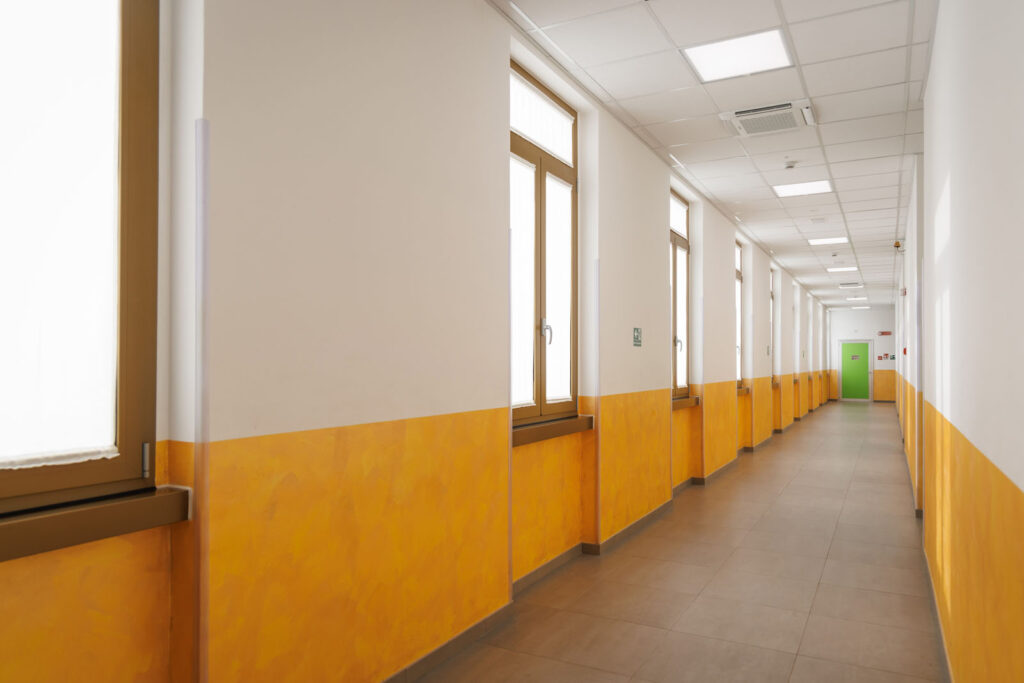 Empty school hallway with orange walls, windows, and green door.