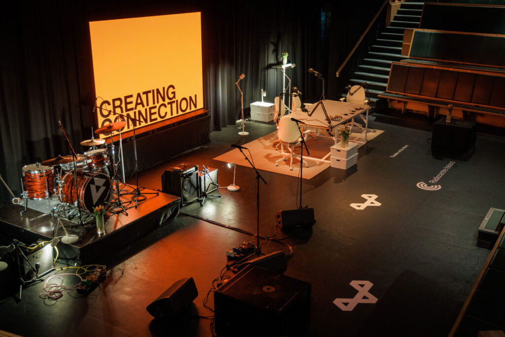 Event stage with drums, podcast setup, and 'Creating Connection' screen.