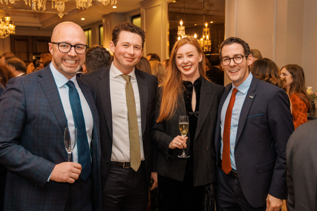 Four smiling people in formal attire at a social event.