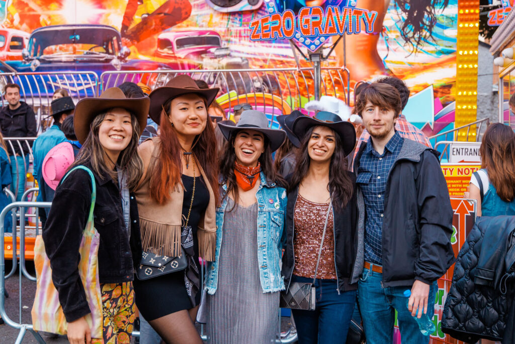 Friends in cowboy hats smiling at a carnival.