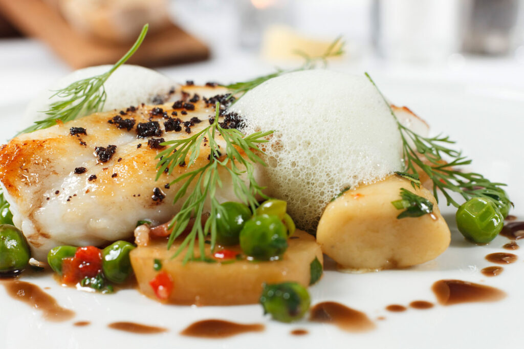 Gourmet fish dish with peas, foam, and sauce.