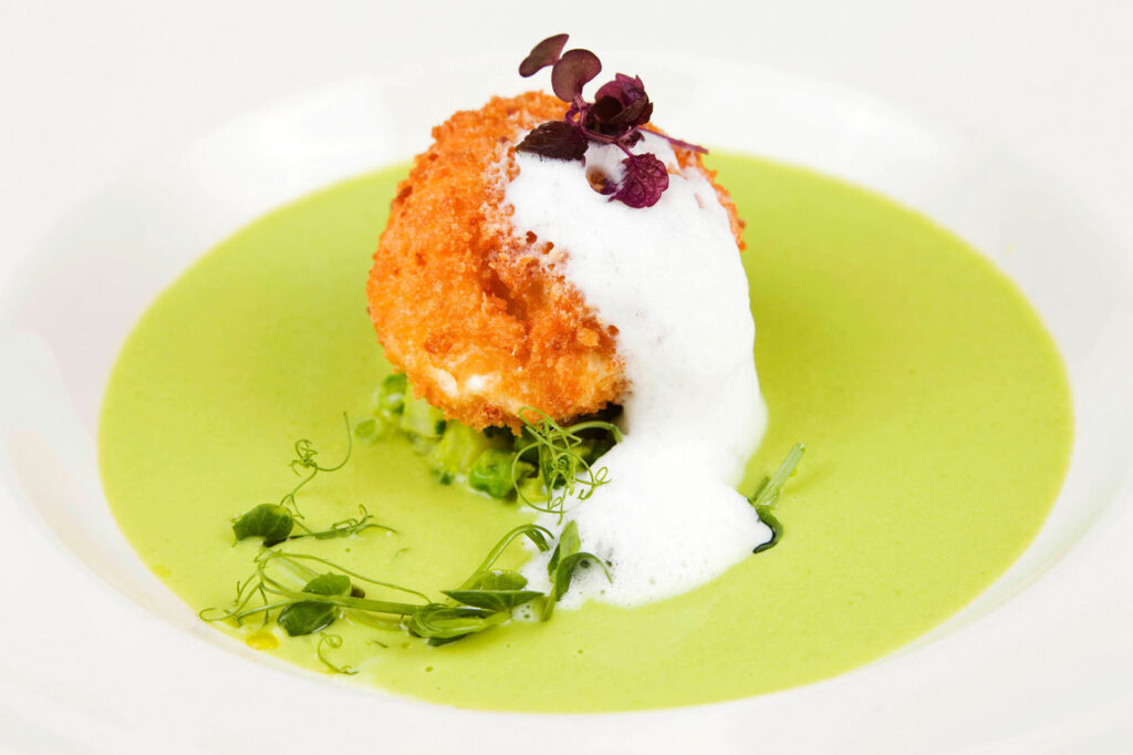 Gourmet fried ball in green soup with foam.