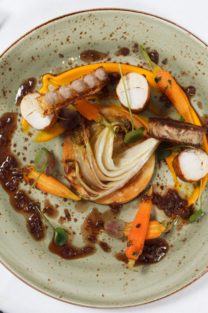Gourmet plated dish with chicken, carrots, endive, and sauces.