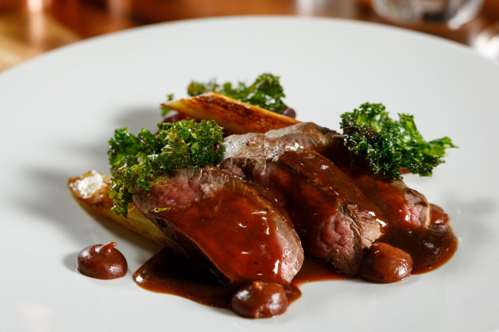 Gourmet sliced meat with rich sauce and kale.