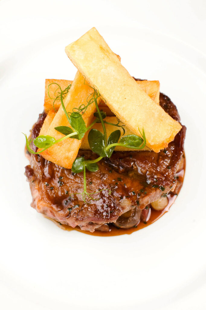 Gourmet steak with thick-cut fries and microgreens on a white plate.