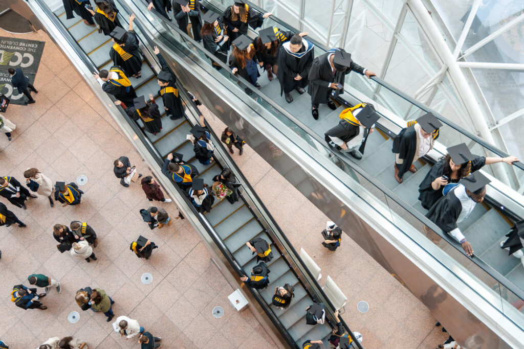 Graduates in caps and gowns on escalators.