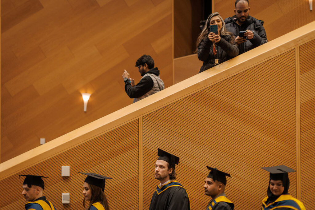 Graduation ceremony: students in gowns, guests with phones.