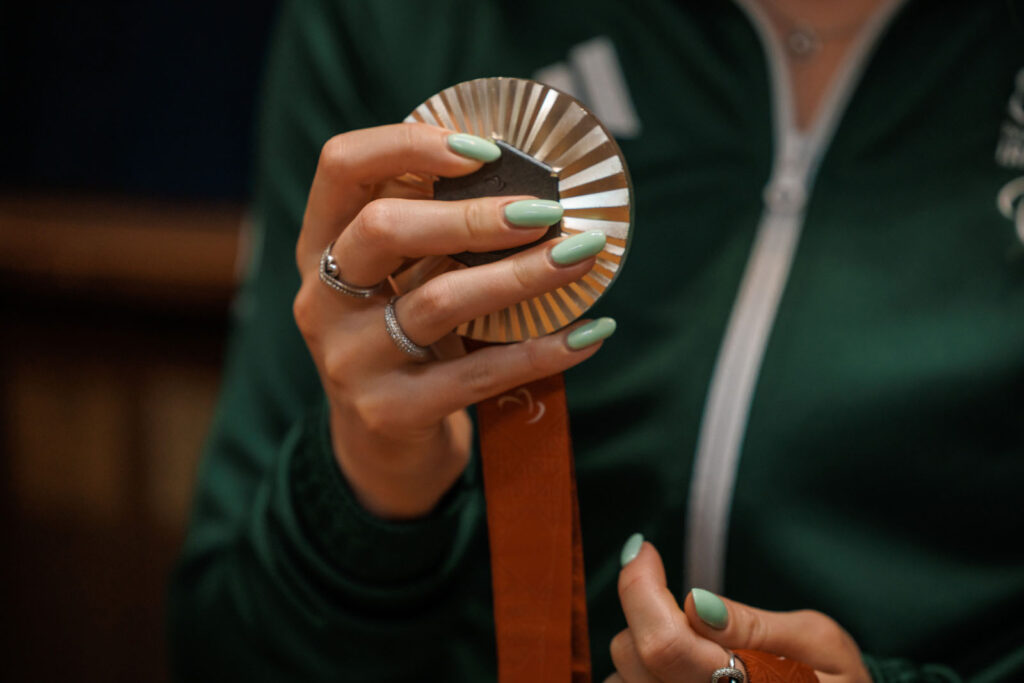 Green-nailed hands proudly display a medal.