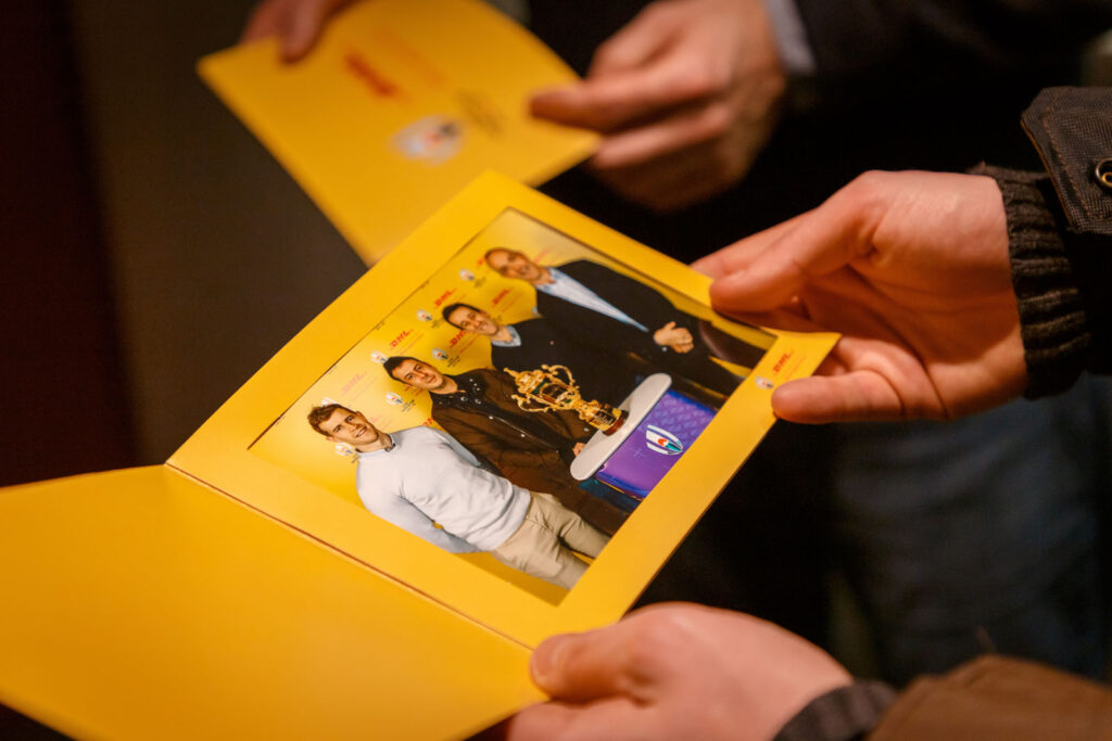 Hands holding photo of men with Rugby World Cup trophy.