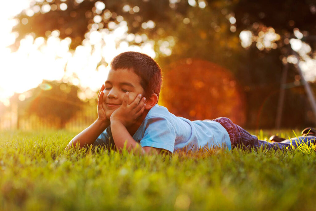 Happy boy relaxing on grass in warm sunlight.