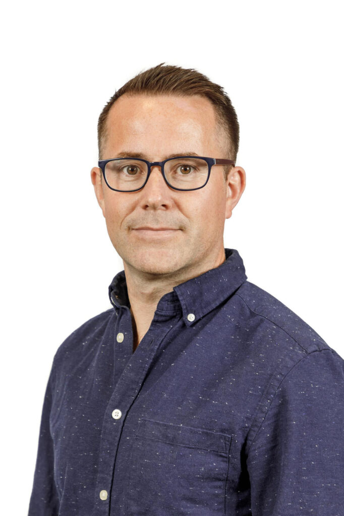 Headshot of a man wearing glasses and a blue shirt.