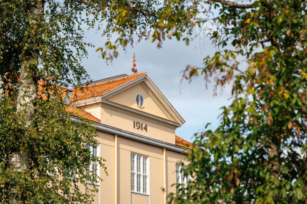 Historic building from 1914, framed by lush green trees.