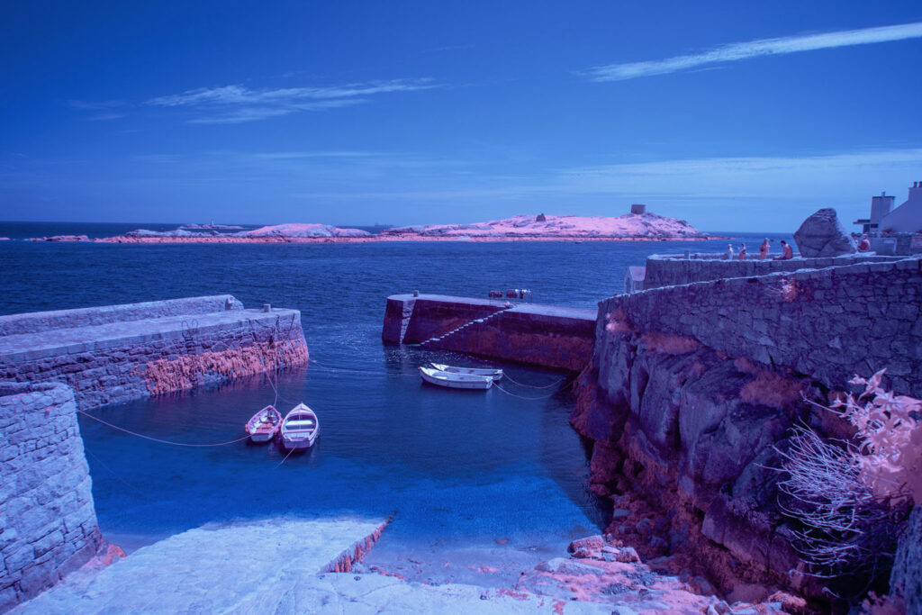 Infrared harbor with boats, stone walls, and island.