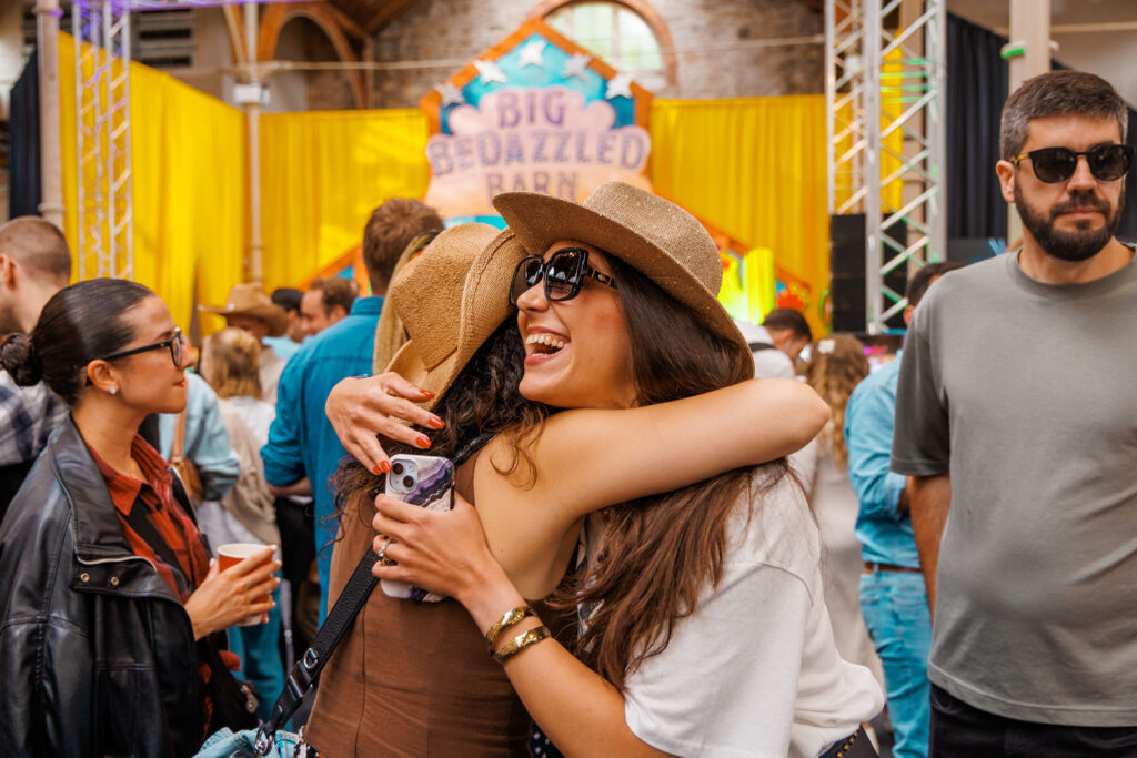 Joyful friends embrace at a crowded indoor event.