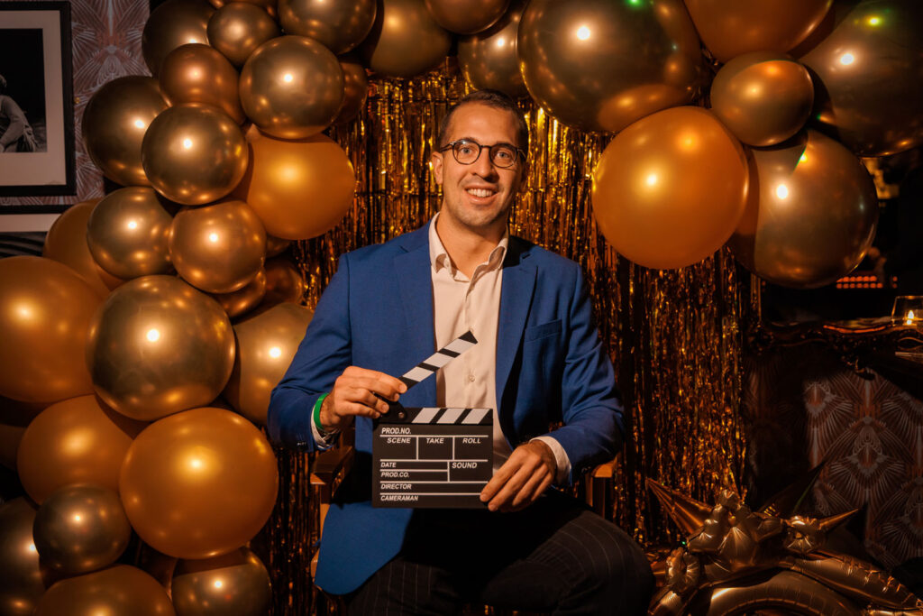 Man holding clapperboard surrounded by golden balloons.