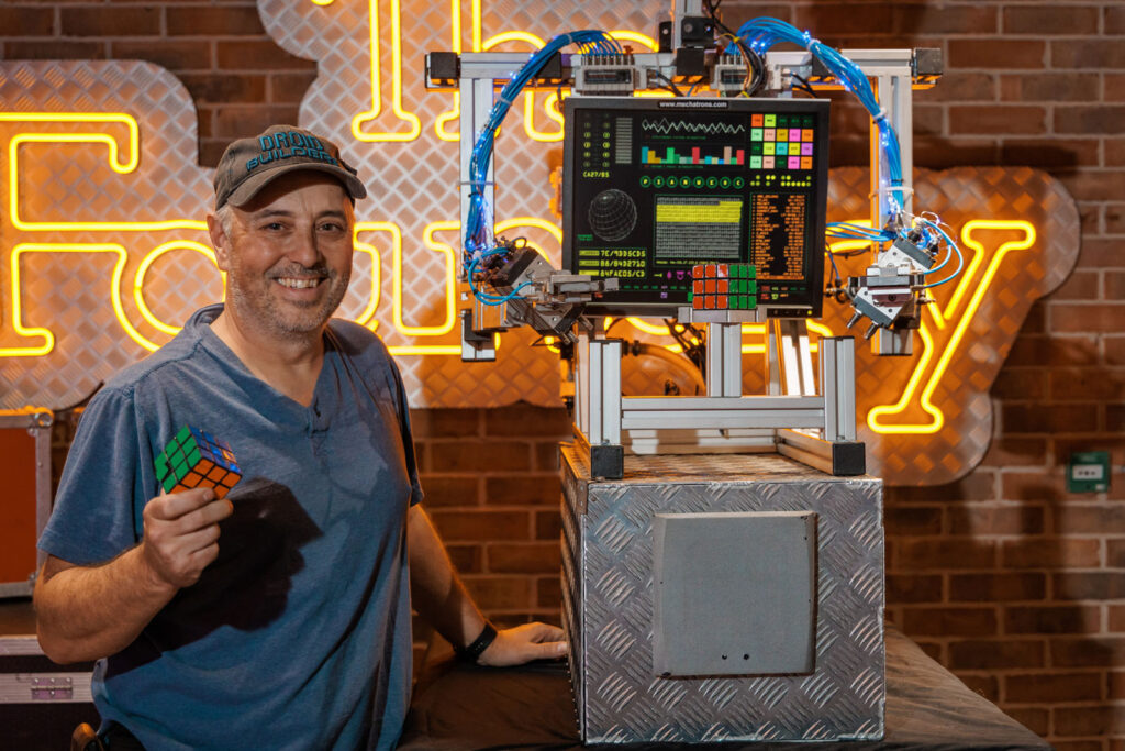 Man holds Rubik's cube next to solving robot.