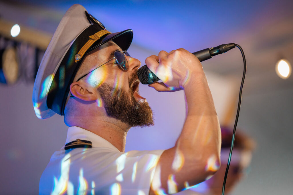 Man in captain's hat singing, colorful light reflections.