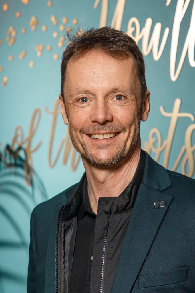 Man in dark suit smiles at camera.