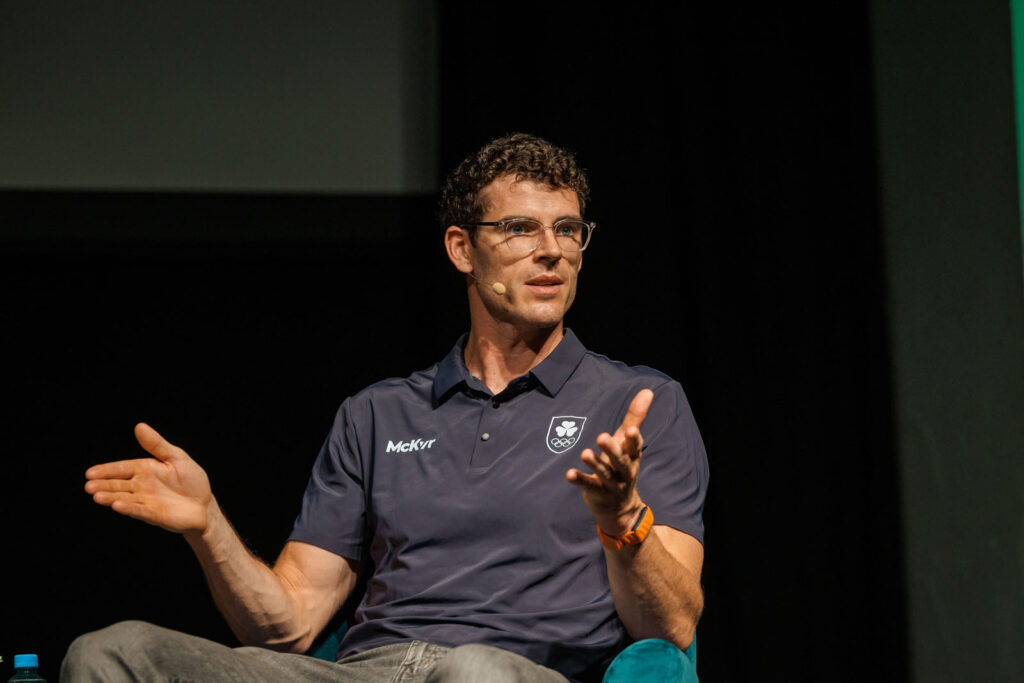 Man in glasses speaking and gesturing at an event.