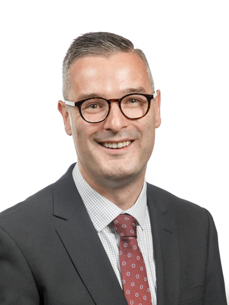 Man in suit and glasses smiling.