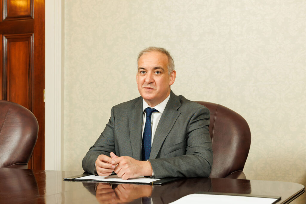 Man in suit sits at conference table.