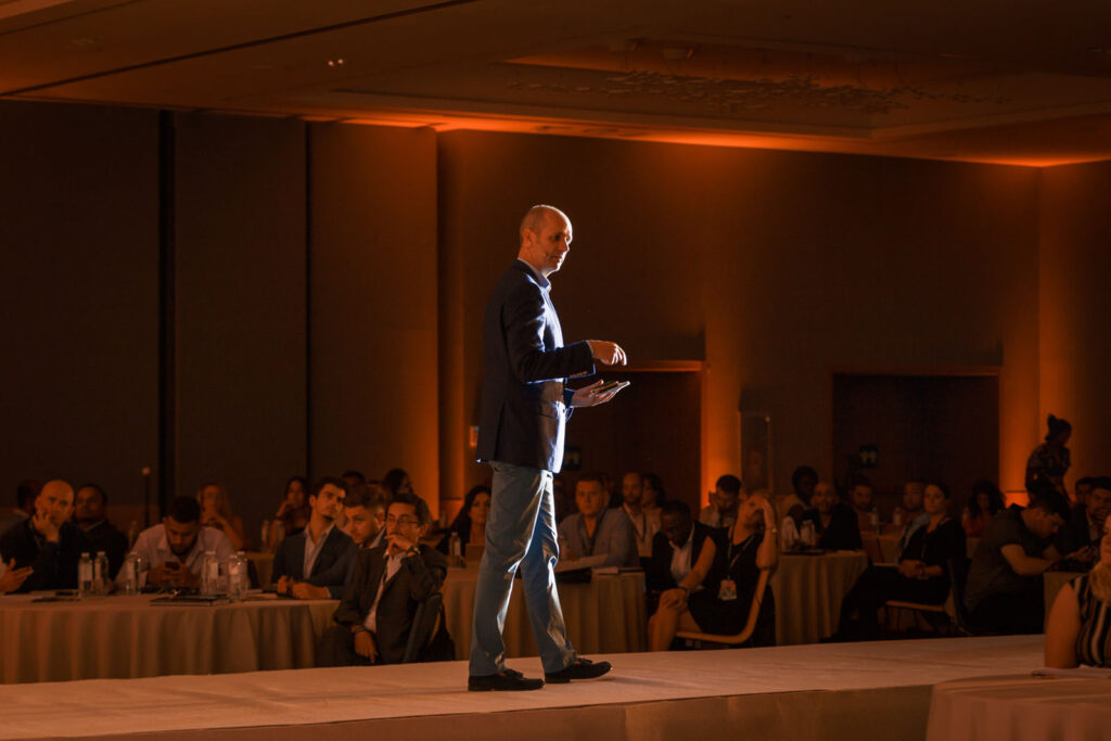 Man presents on stage to an audience at a conference.