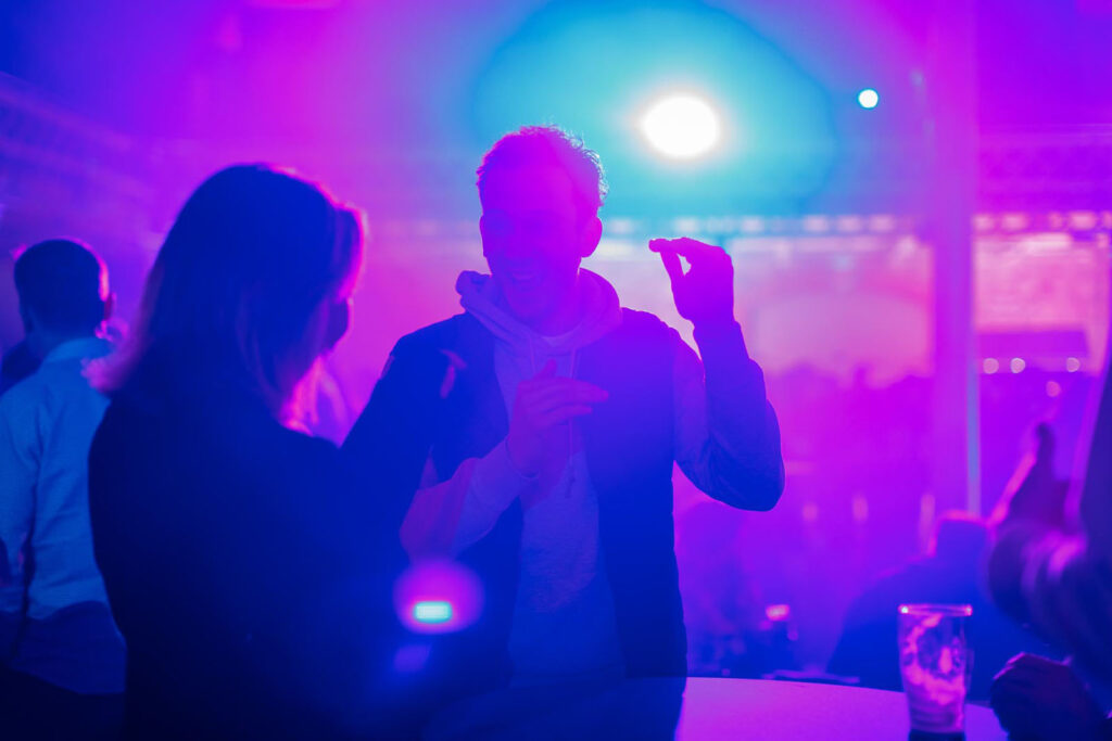Man smiling and dancing in a club with colorful lights.