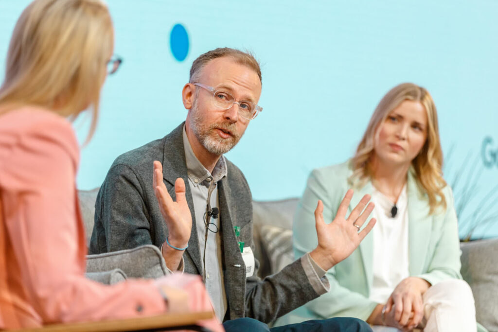 Man with glasses speaking animatedly at a conference panel.