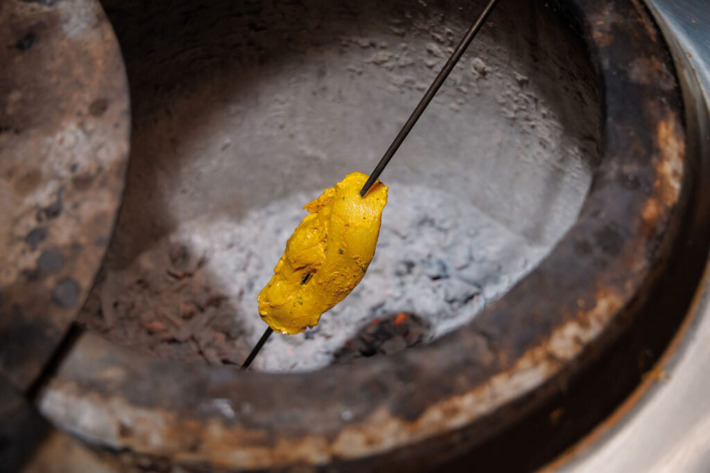 Marinated chicken cooking on a skewer in a tandoor oven.