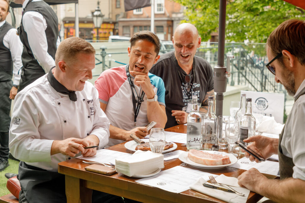 Men laughing at outdoor steak tasting event.