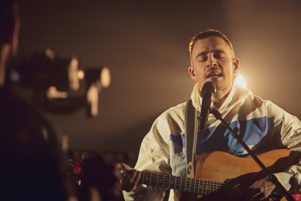 Musician performs live, singing and playing acoustic guitar.