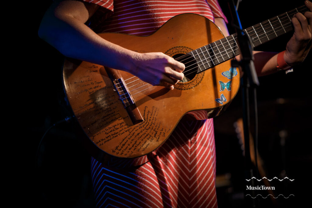 Musician playing acoustic guitar with handwritten lyrics and butterfly stickers.