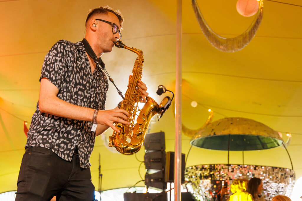 Musician plays saxophone under a yellow tent.