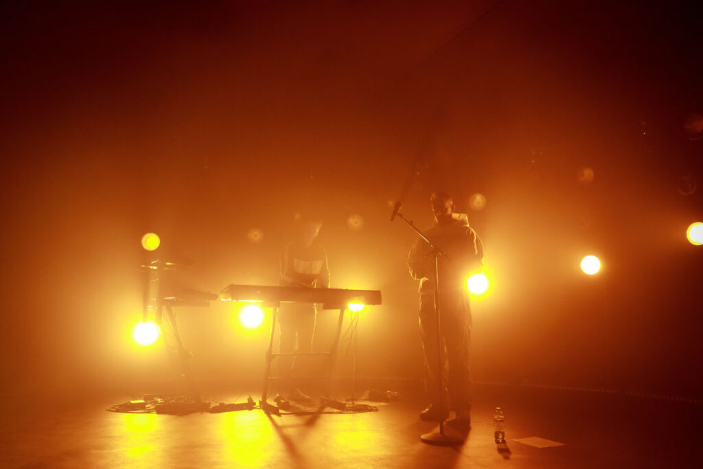 Musicians perform on stage bathed in warm, hazy light.